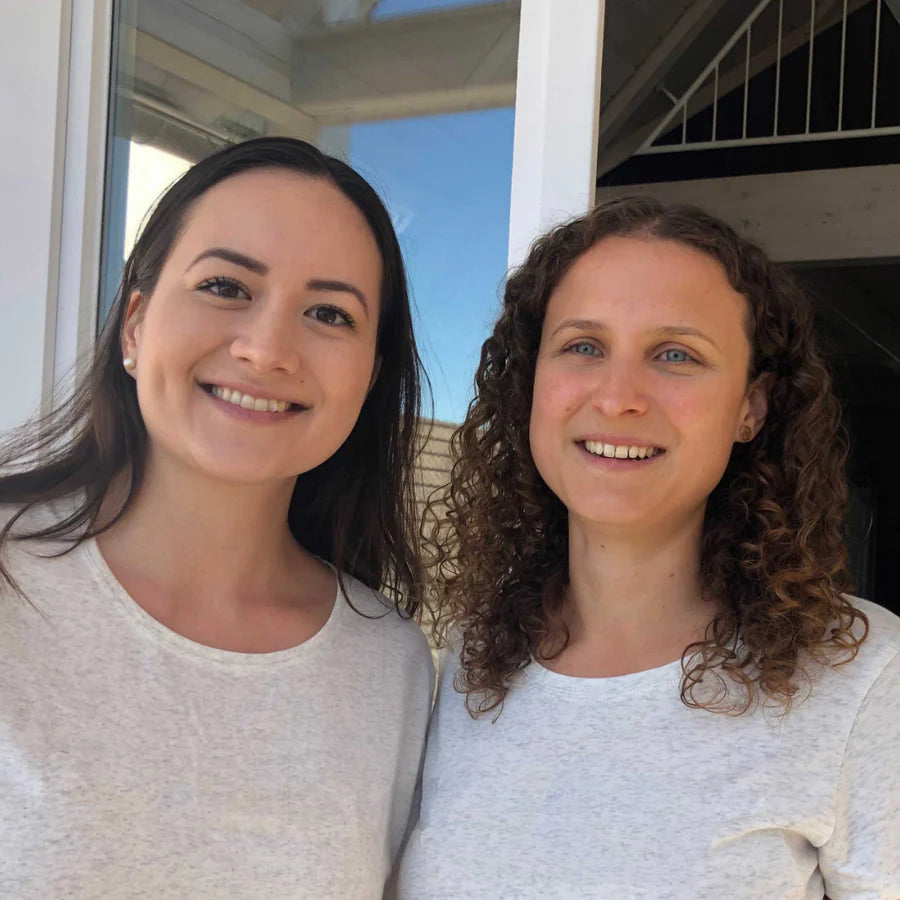 Two dark haired women in grey tops standing close to each other. Olivia & Lena - Kinderzimmer.de