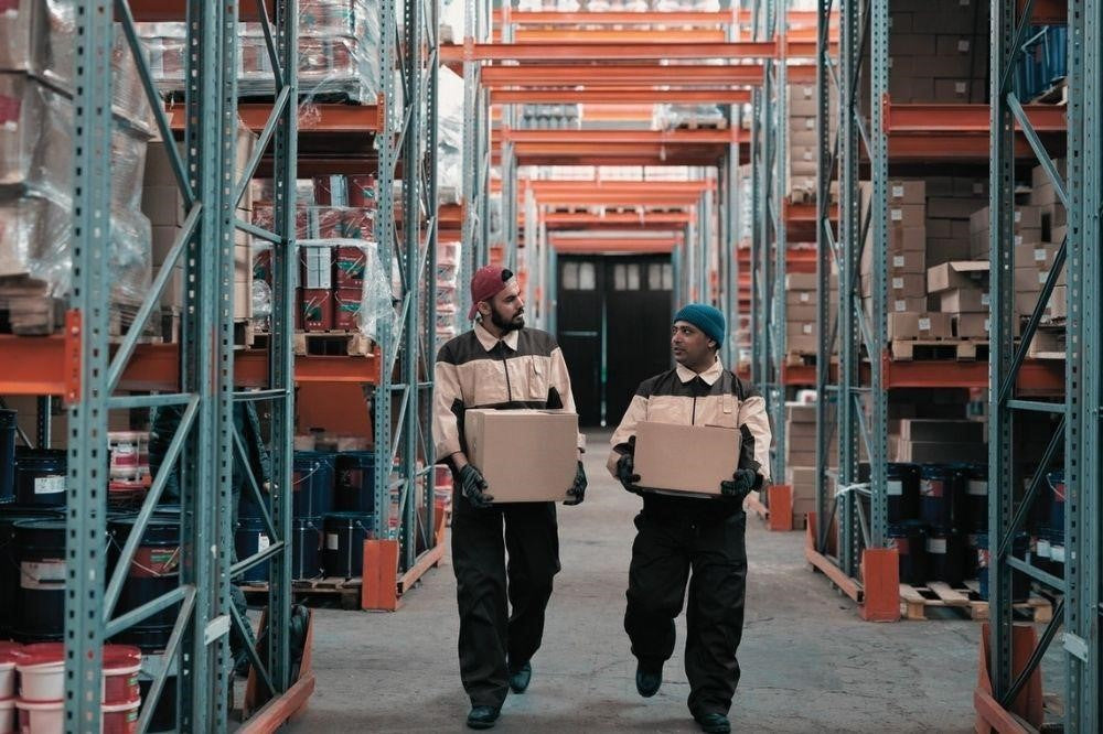 Two warehouse men looking at each other while holding two boxes